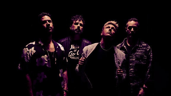 Die vier Band-Mitglieder von Papa Roach in spärlicher Beleuchtung und rockiger Klamotte
