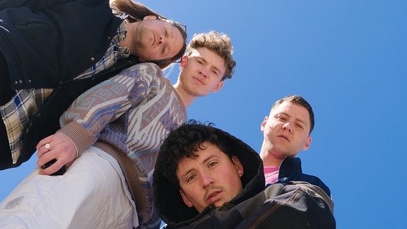 die vier Bandmitglieder von Provinz schauen von oben nach unten in die Kamera vor blauem Himmel