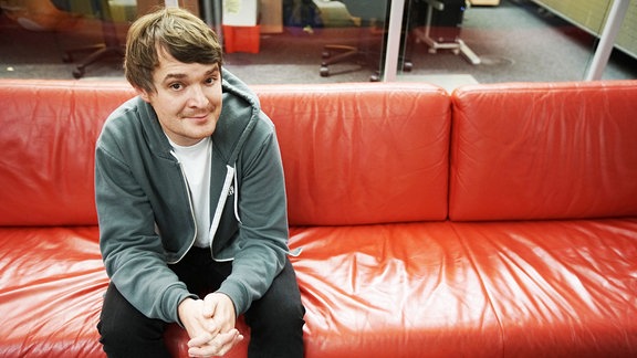 Sebastian Madsen sitzt auf dem roten SPUTNIK-Sofa